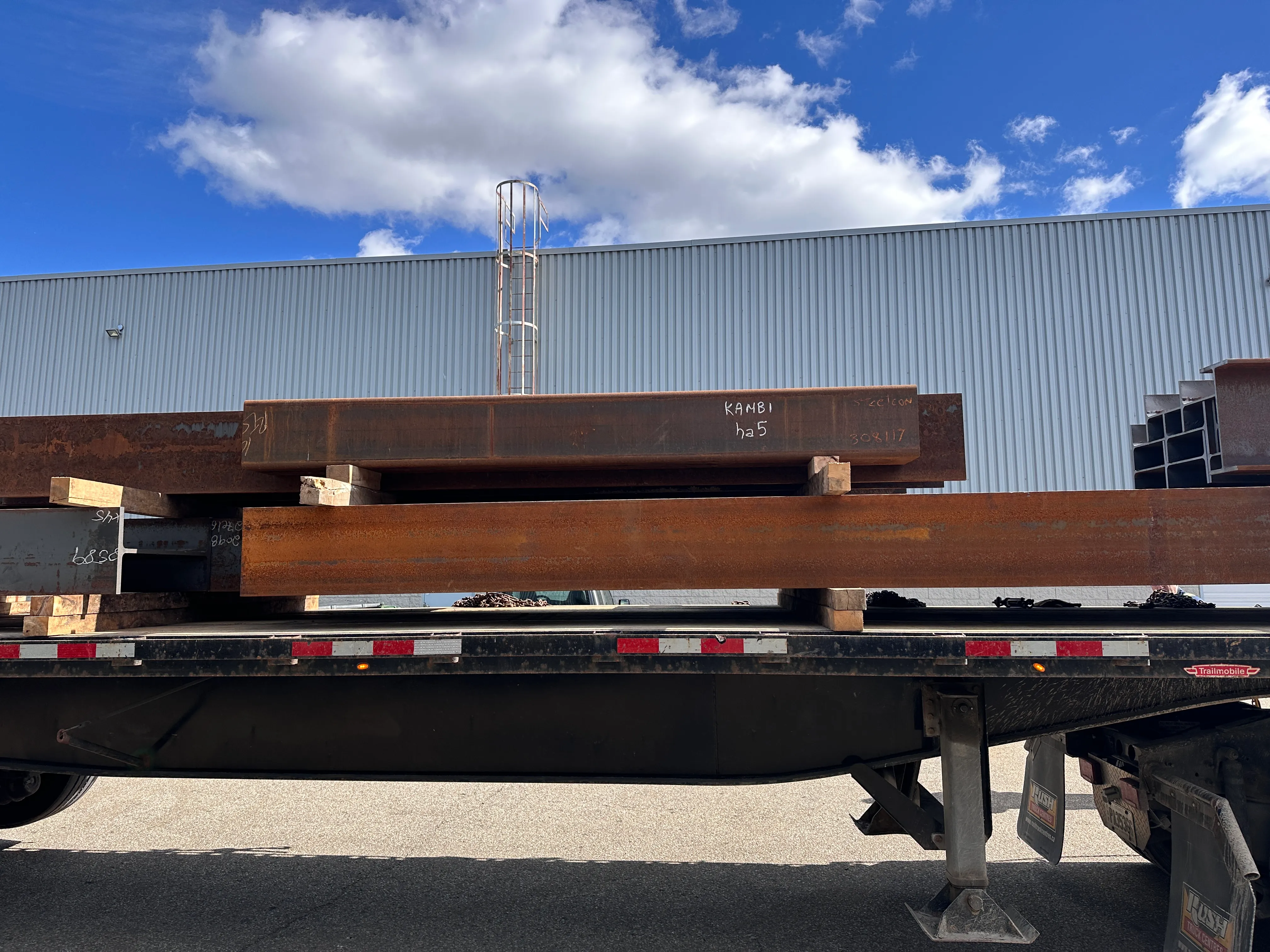 Structural steel members marked for Kambi loaded on a flatbed trailer for delivery.